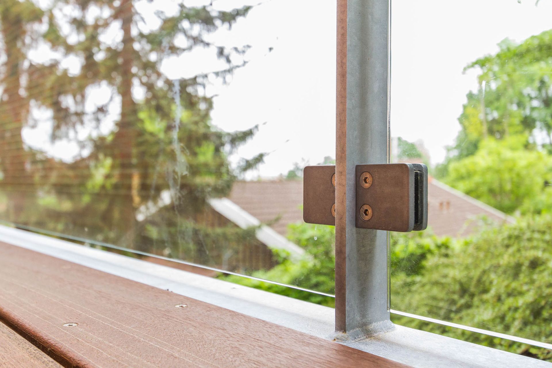 Et nærbillede af et glasrækværk på en balkon med træer i baggrunden.
