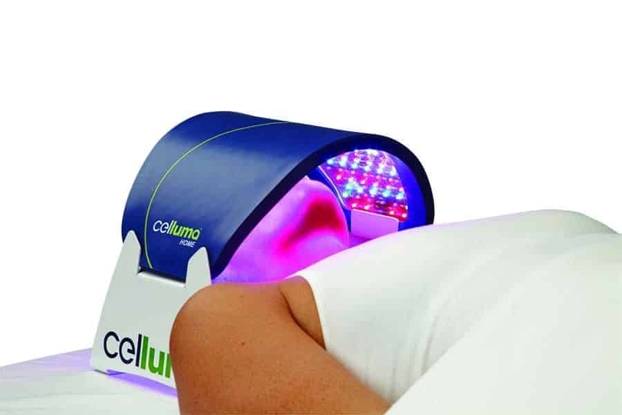 A person lying under a blue Celluma LED light therapy machine, undergoing a treatment.