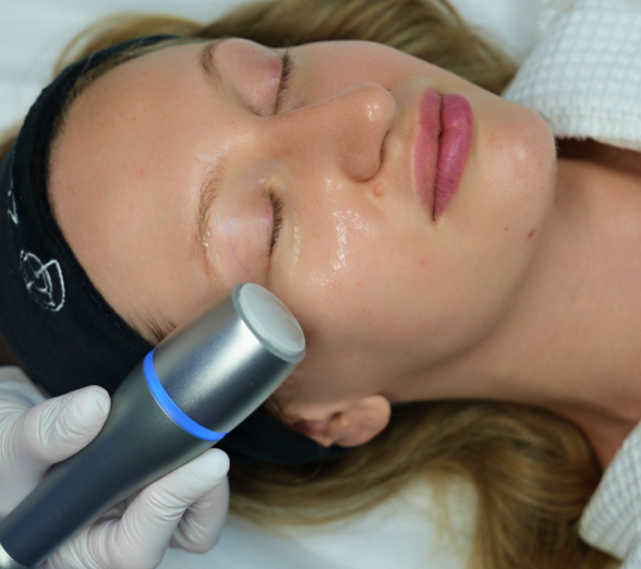 Woman undergoing facial treatment with a handheld device, eyes closed, in a spa setting.