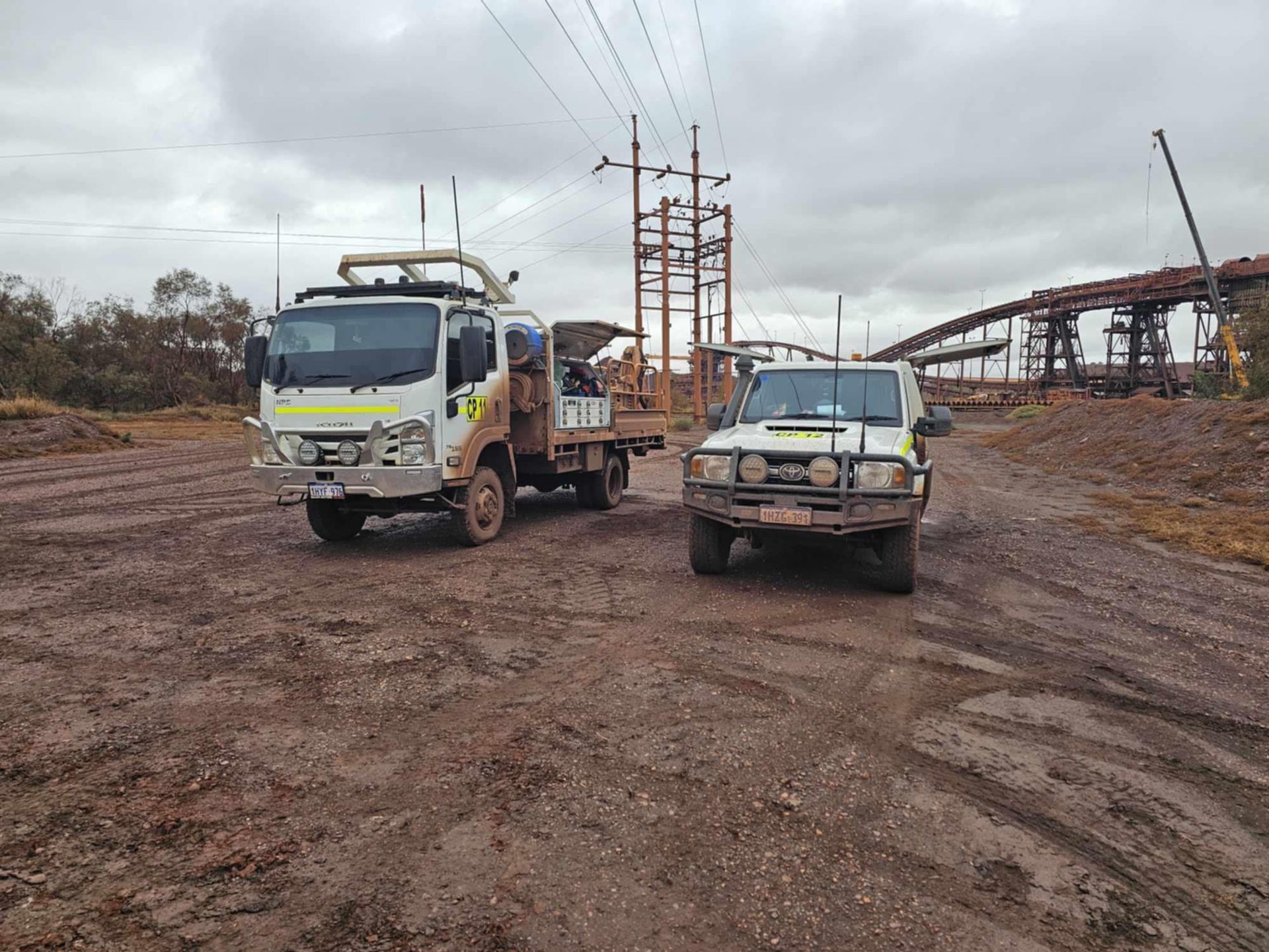 Two trucks are parked next to each other on a dirt road.