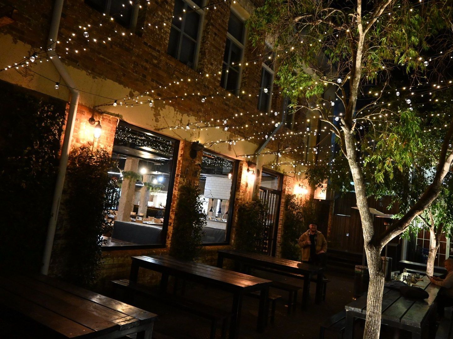 A group of tables and benches outside of a building at night.