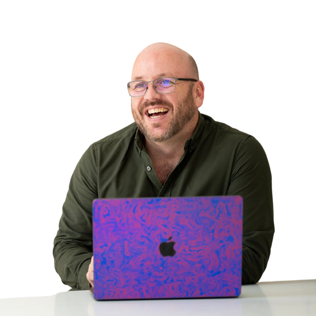 A man is smiling while sitting in front of an apple laptop