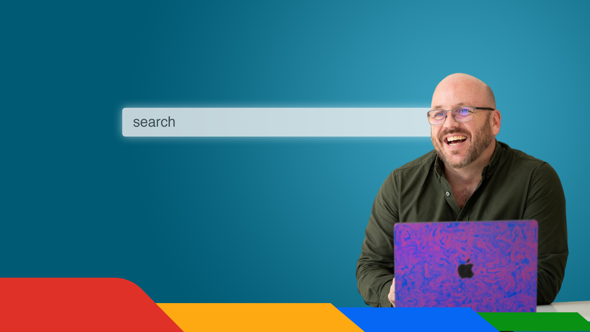 A man is smiling while sitting in front of an apple laptop