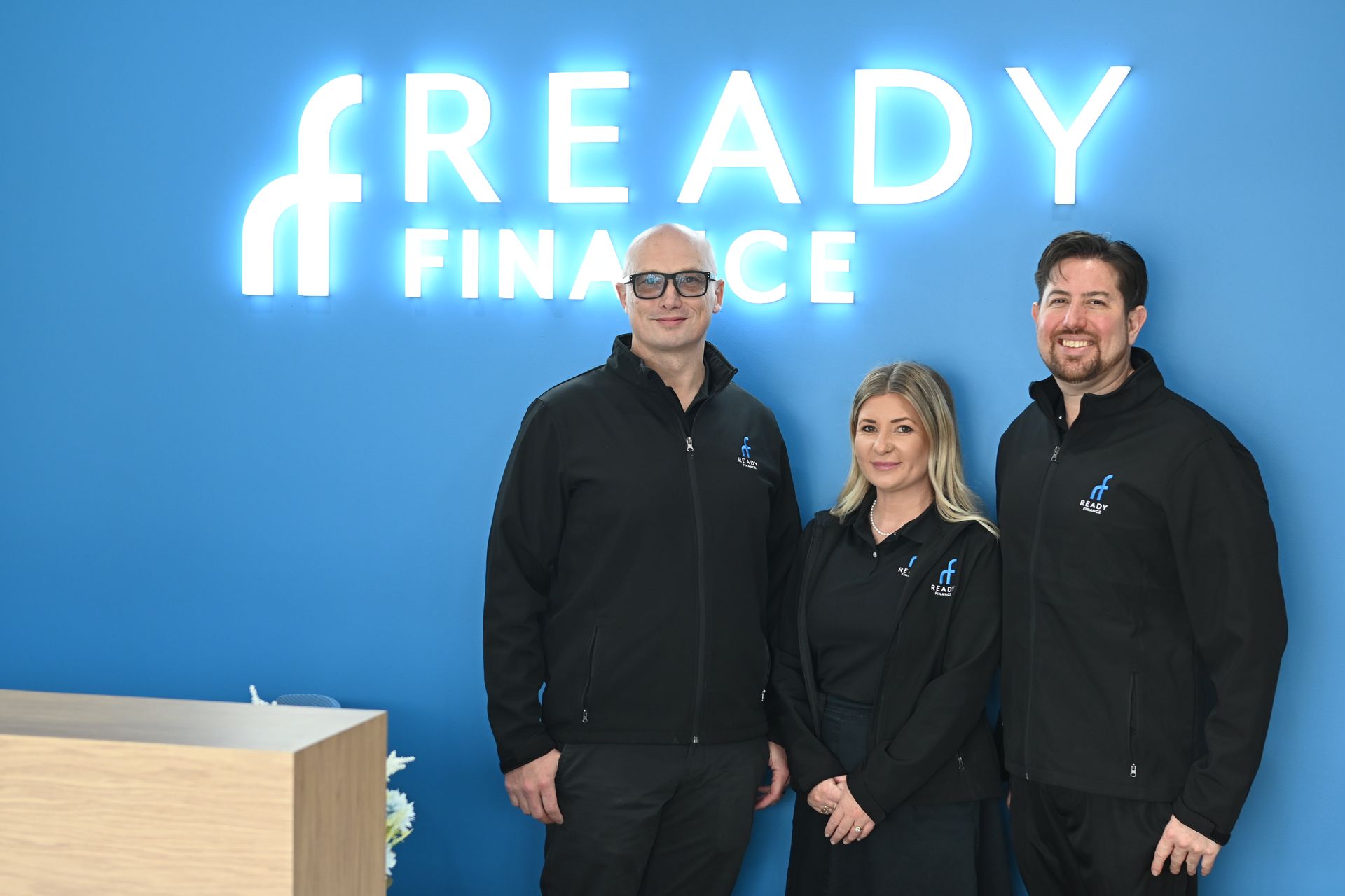 Three people are standing in front of a sign that says ready finance.