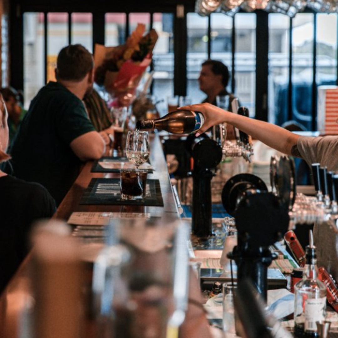 A group of people are sitting at a bar drinking beer