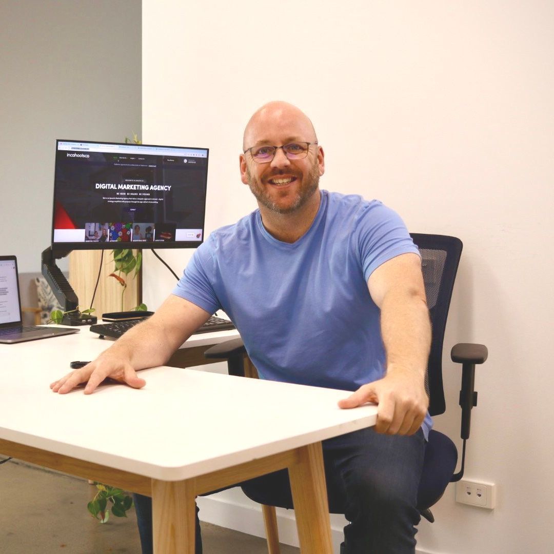 A man in a blue shirt is sitting at a desk in front of a computer monitor