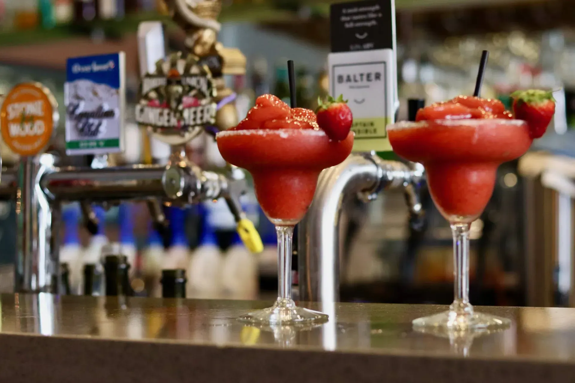 Three strawberry margaritas are sitting on a bar counter.