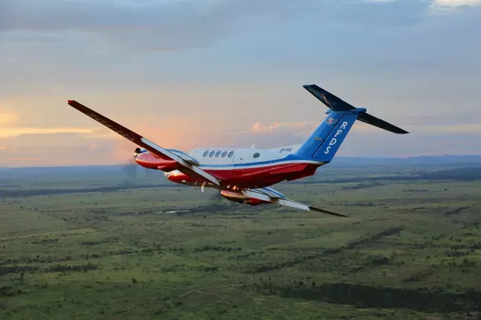 Airplane flying over a green landscape with a sunset sky in the background.