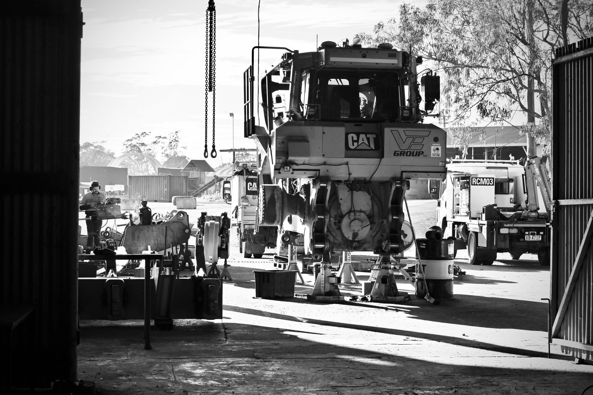 A large Caterpillar truck being worked on in an industrial yard; several people, machinery.