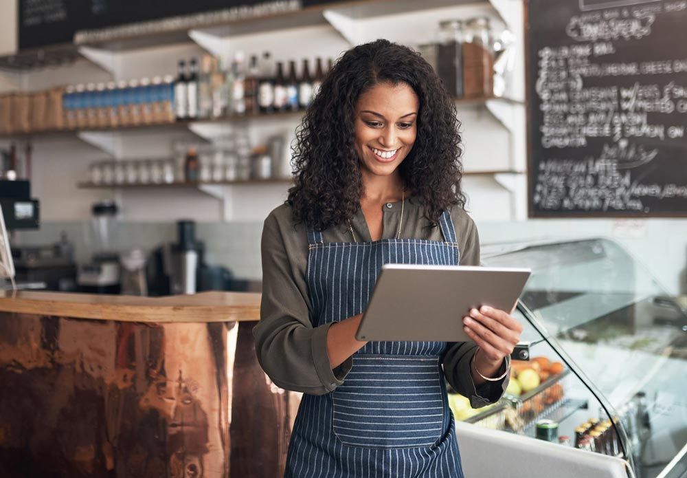 A woman in an apron is looking at a tablet in a restaurant.