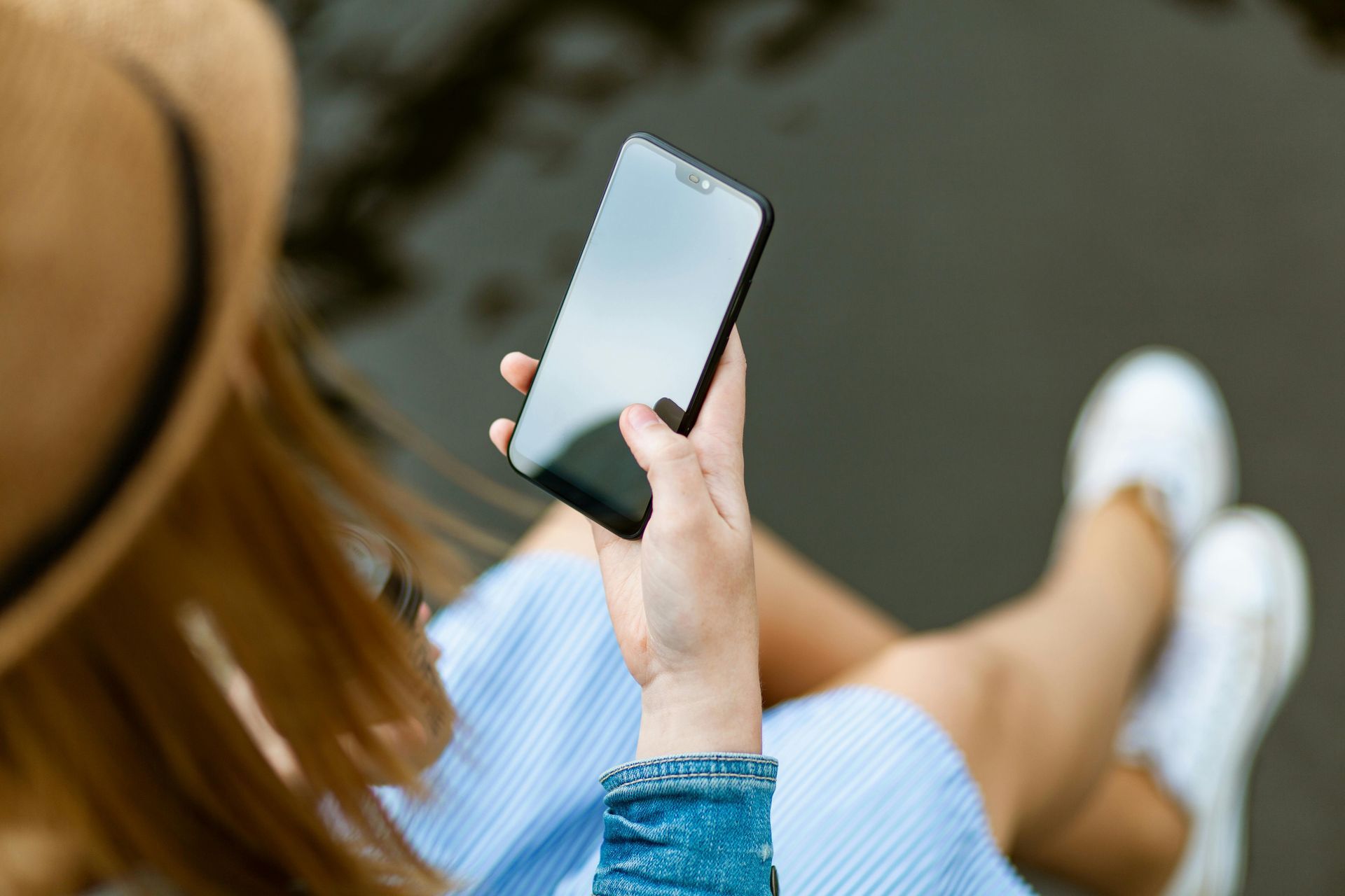 A woman wearing a hat is holding a cell phone in her hand.