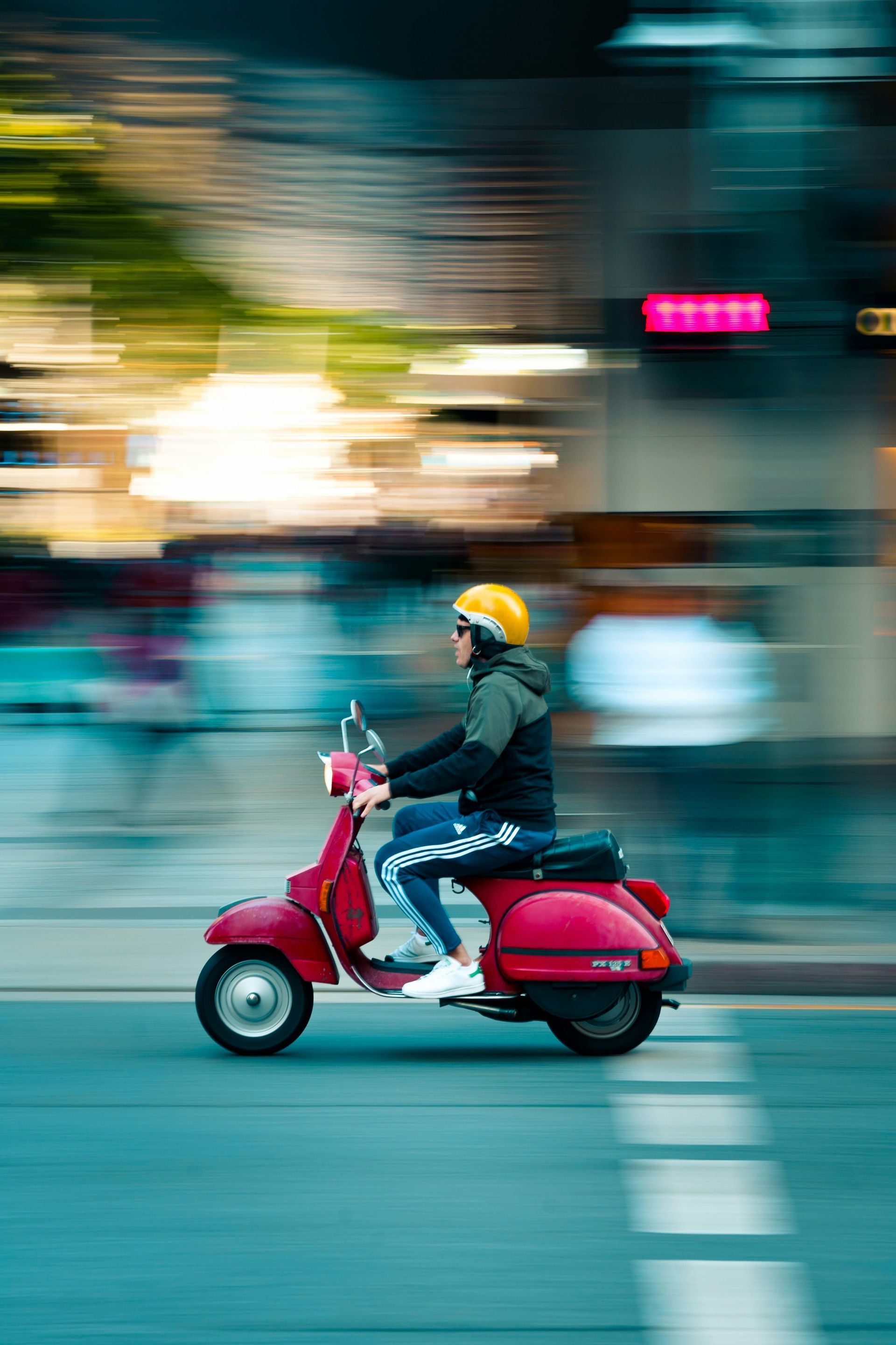 A man is riding a red scooter down a city street.