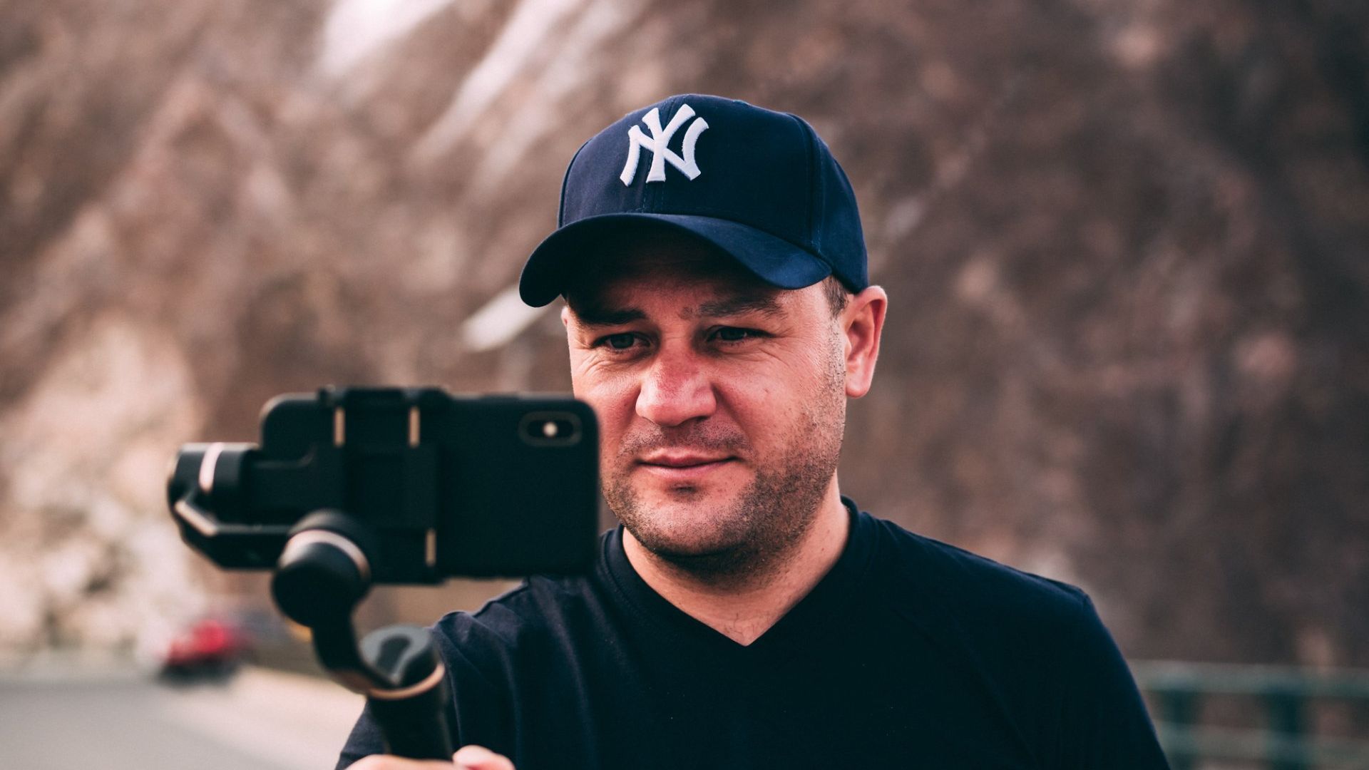 A man wearing a ny hat is taking a picture with a cell phone.