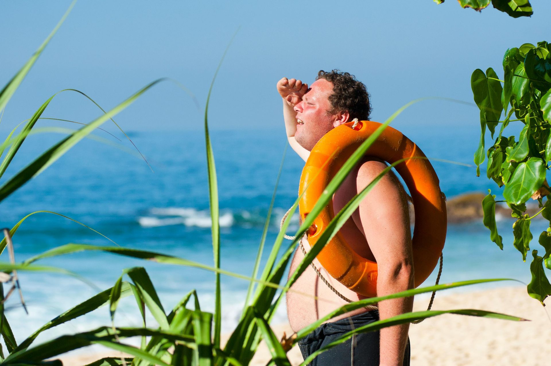 A man with a life preserver around his neck is standing on a beach