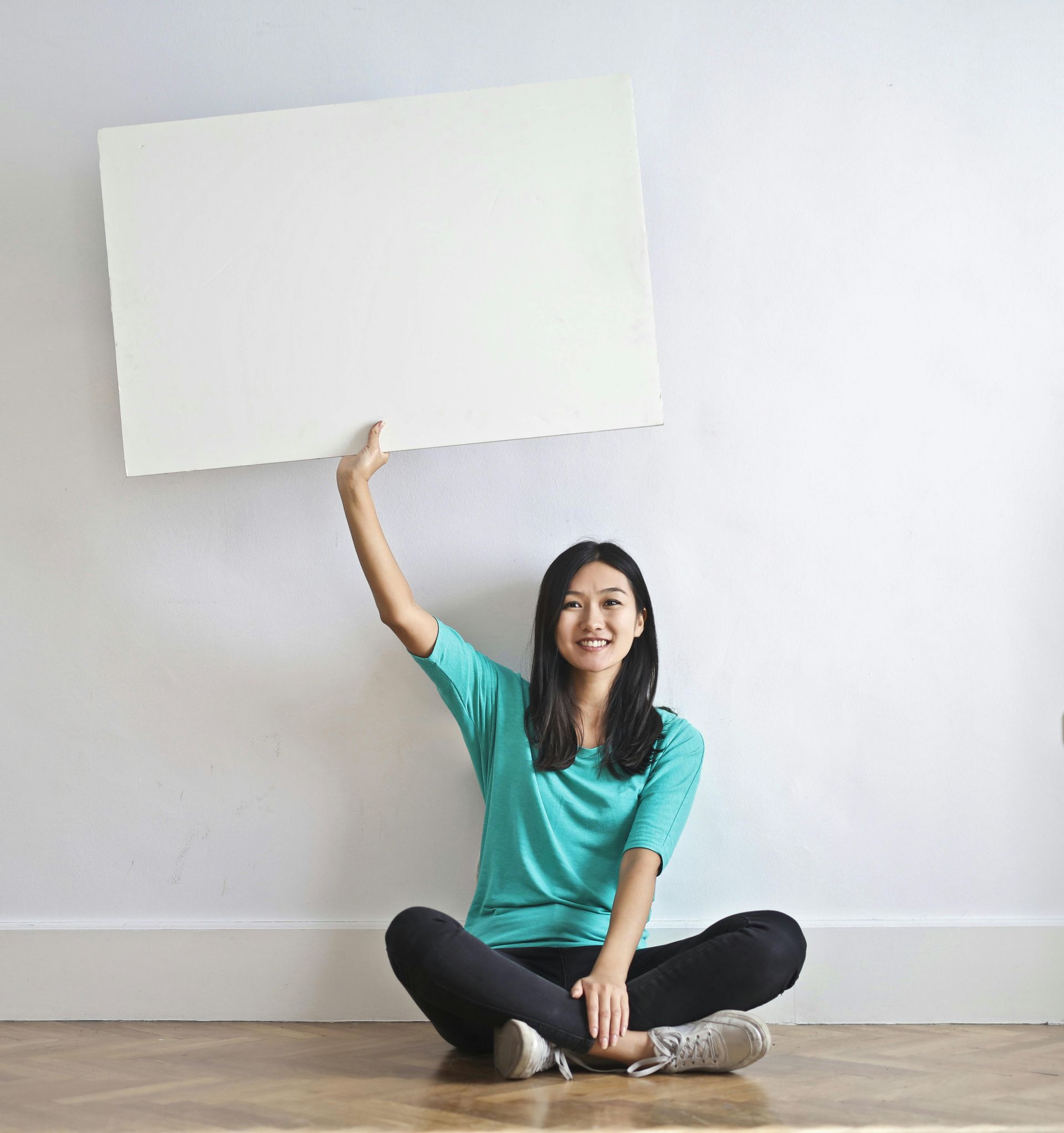 A woman is sitting on the floor holding a white sign.