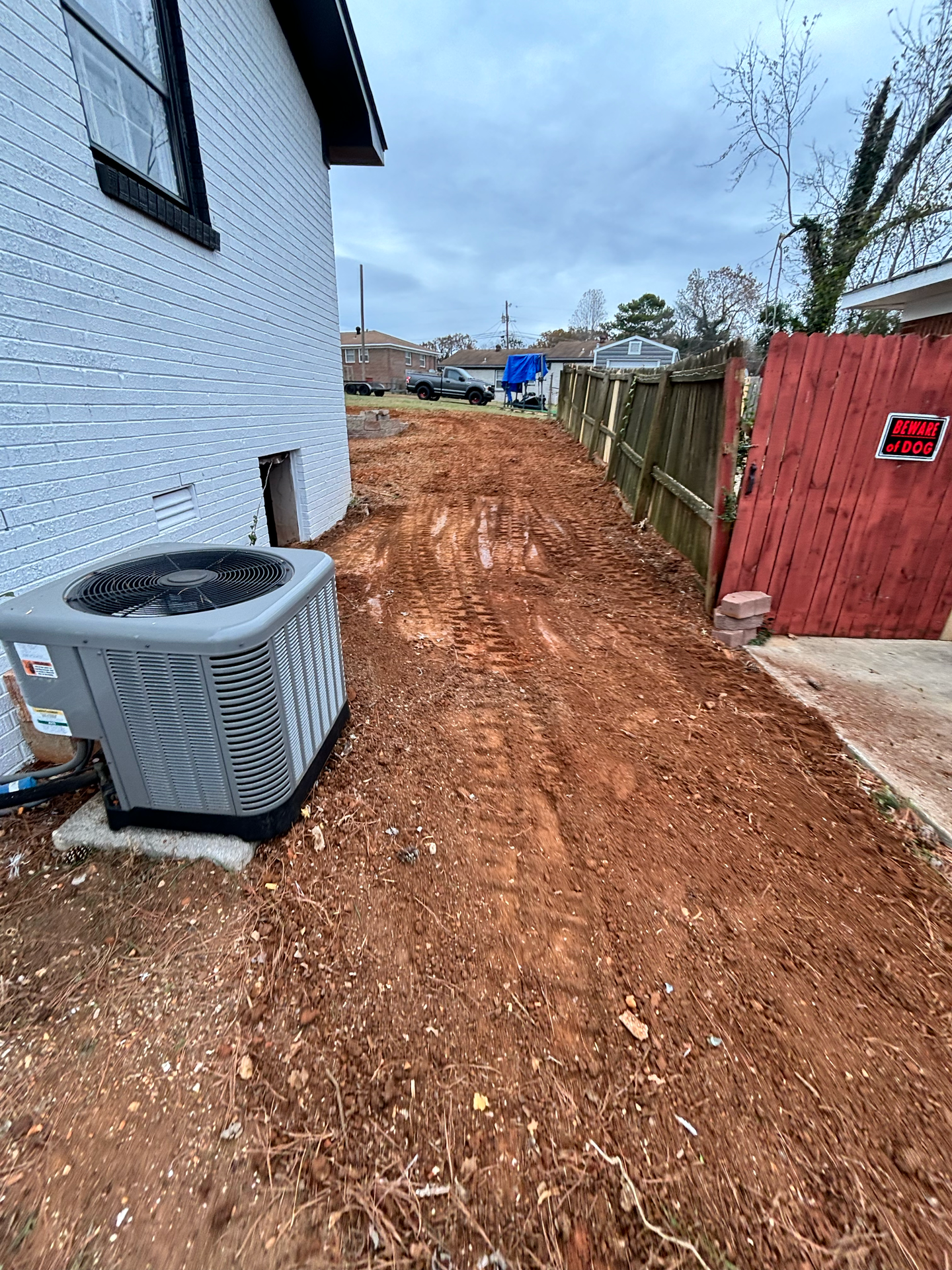 An air conditioner is sitting on the side of a dirt road next to a house.