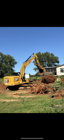 A large yellow excavator is digging a pile of dirt in a field.