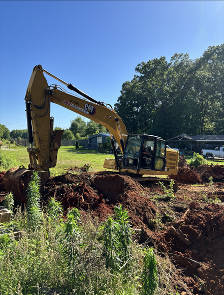 A cat excavator is digging a hole in a field.