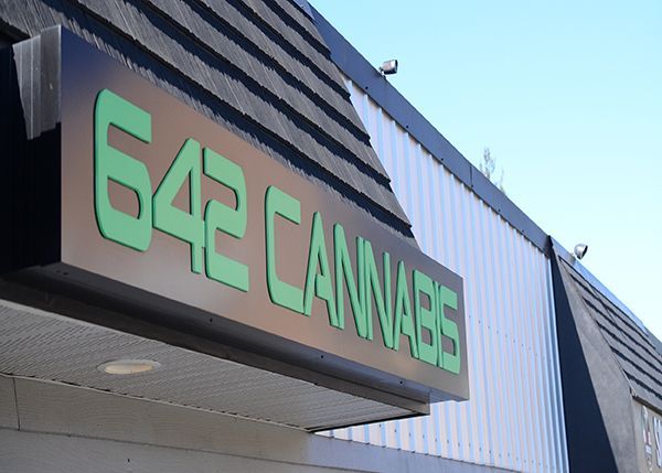 Sign for 642 Cannabis, green letters on black, mounted on building with black and white siding.