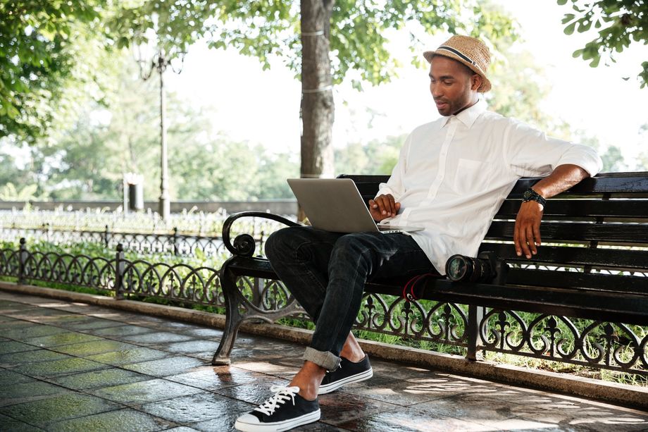 A man is sitting on a park bench using a laptop computer.