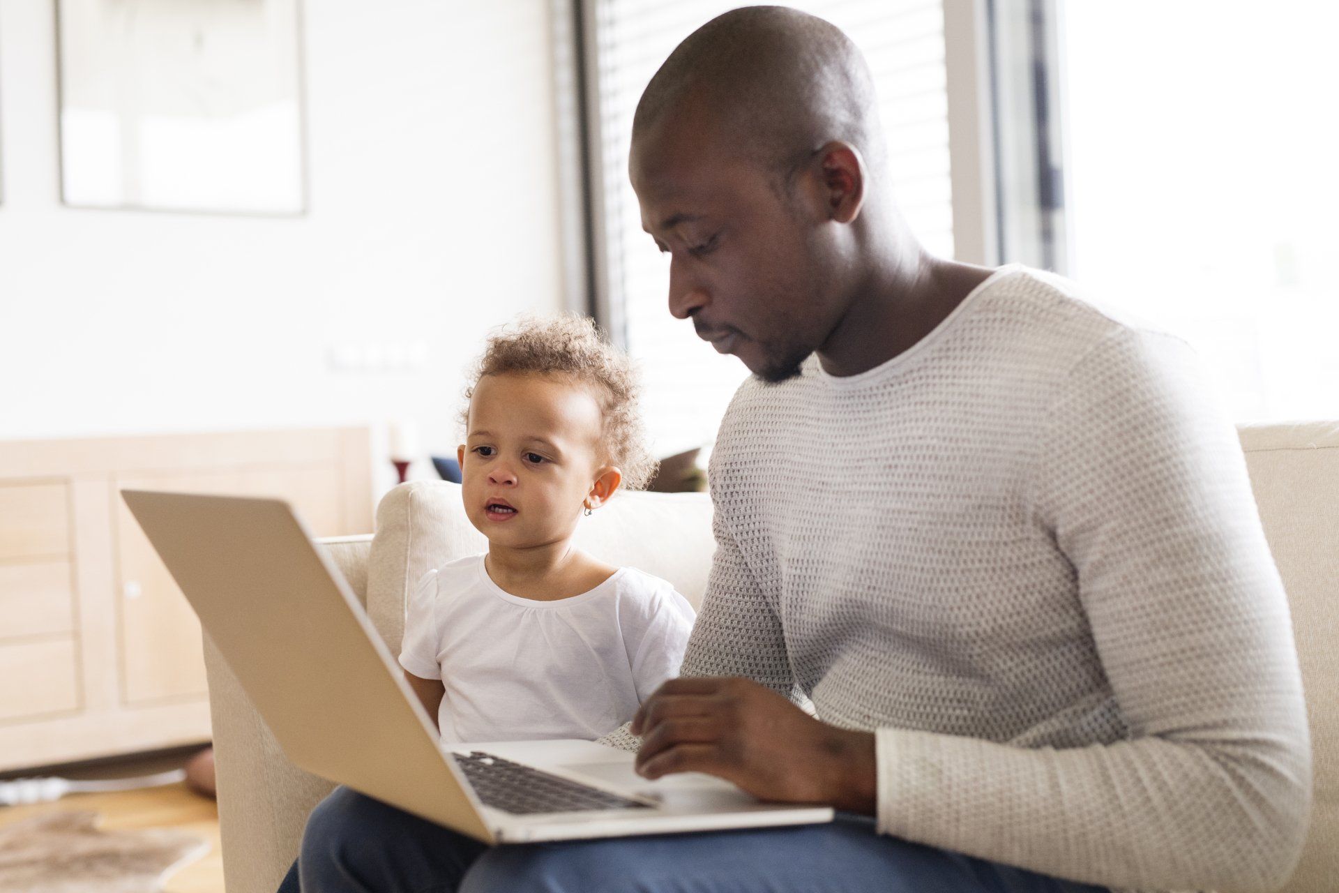 A man and a child are sitting on a couch using a laptop computer.