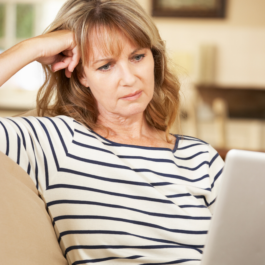 A woman in a striped shirt is sitting on a couch looking at a laptop