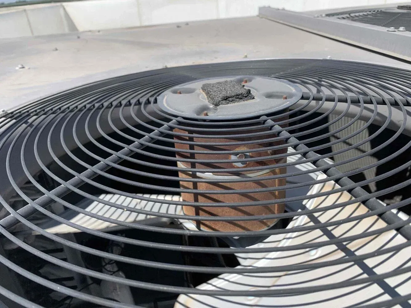 A black metal fan grill on top of a rooftop air conditioning unit, featuring a weathered circular motor housing.