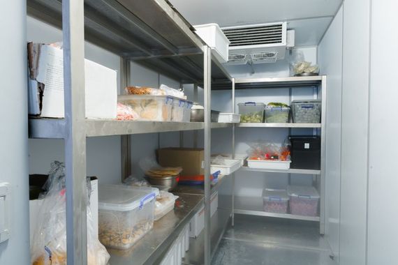 A walk-in commercial refrigerator with metal shelving holding various food containers and supplies.