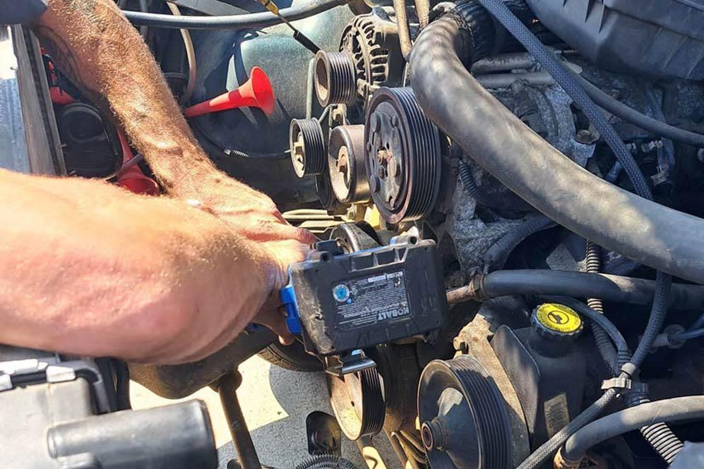 Person working on an engine, accessing parts near belts and pulleys.