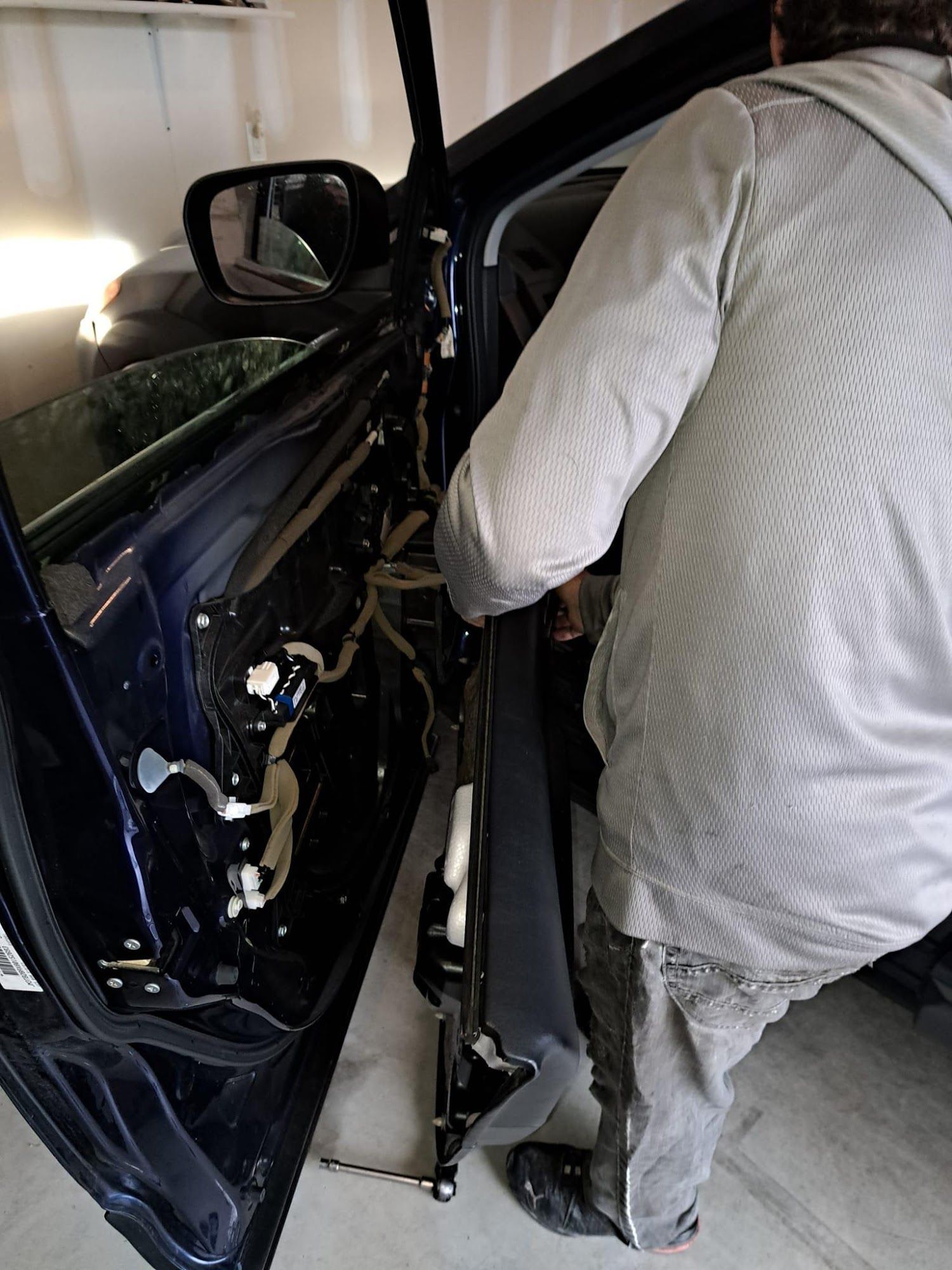 Person working on a car door, removing components. Visible wires, blue car, gray clothing.