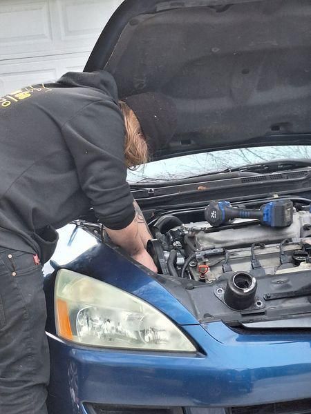 Person working on a blue car engine with hood open; using tools.
