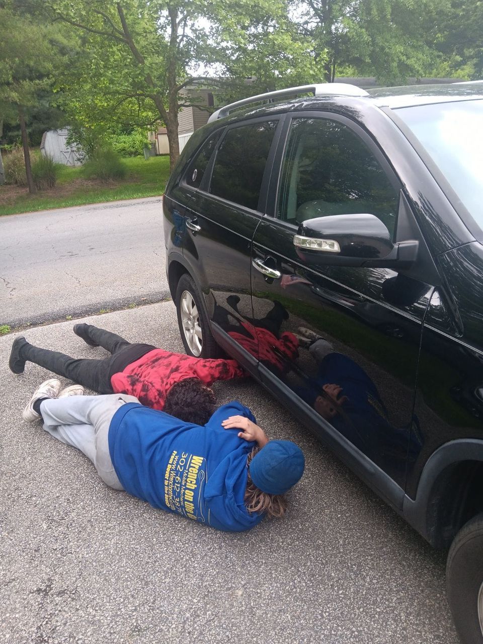 Three people lying on pavement next to a black SUV.