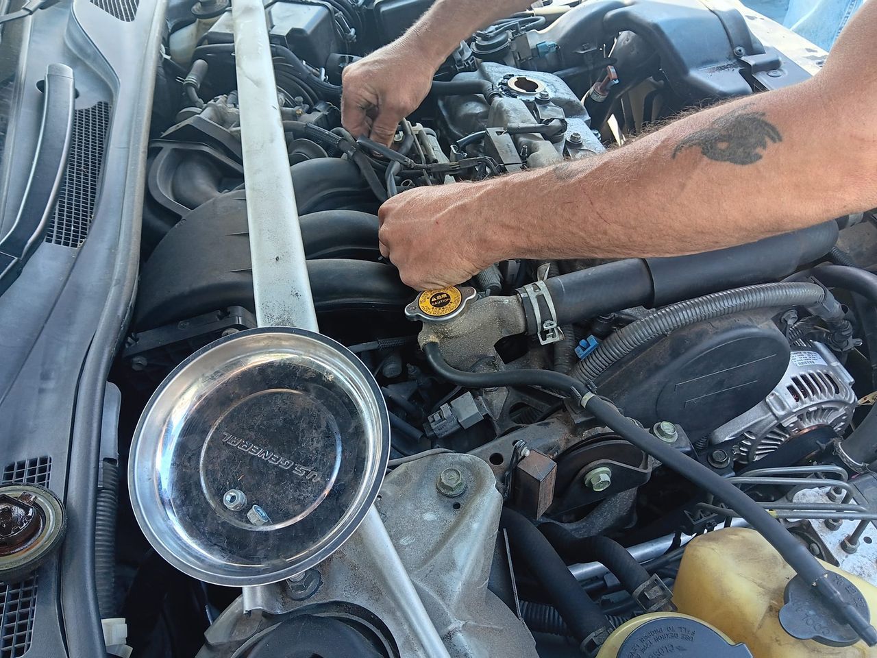 Hands working on a car engine, tools visible, outdoors, daytime.