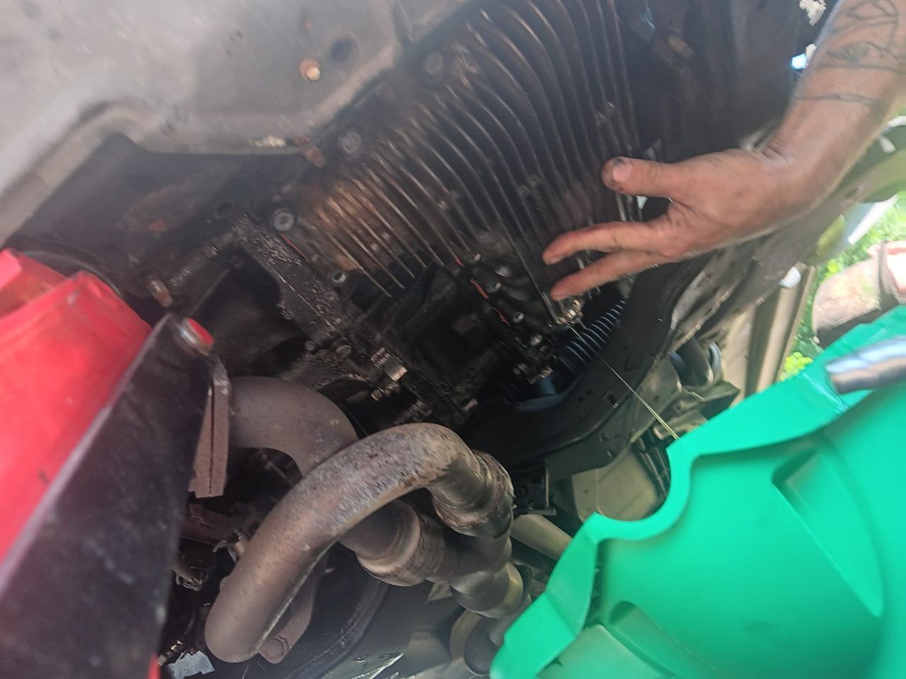 A person working on a car engine; oily engine parts visible, hand touching the top.