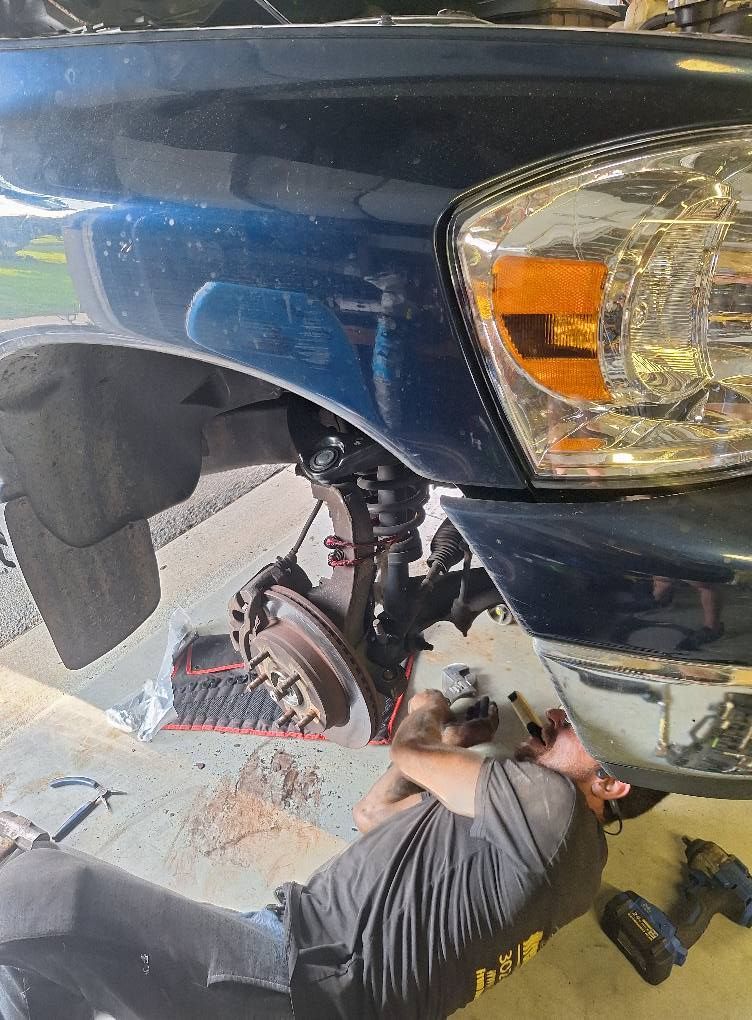 Mechanic working on the front suspension of a blue truck, lying on the ground.