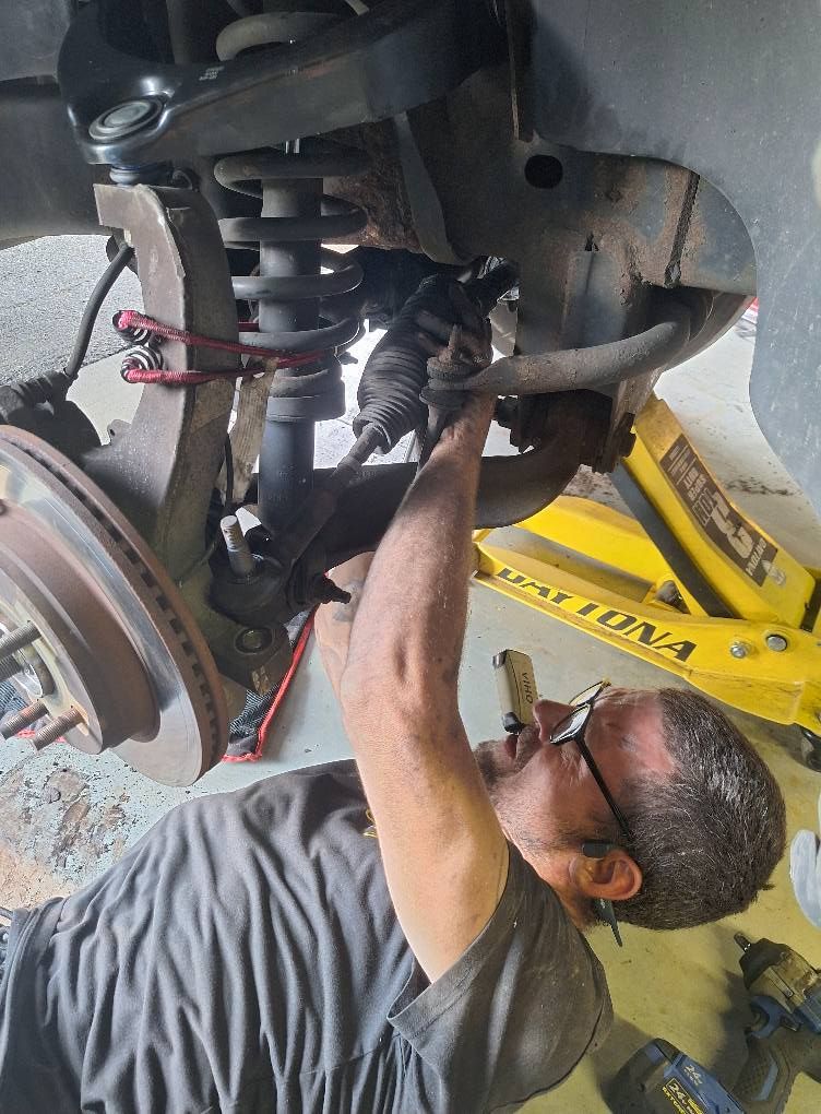 Mechanic working on car suspension; lying on back, using tools. Yellow jack supporting vehicle.