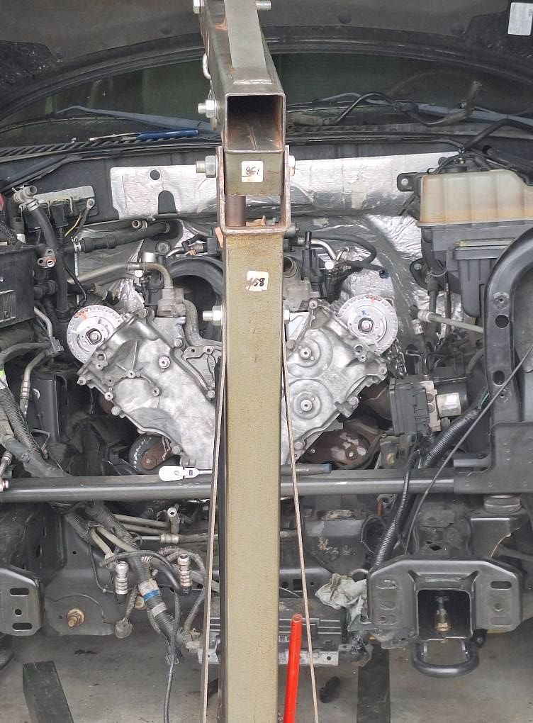 An engine hoist supporting an exposed car engine; the vehicle is undergoing maintenance.