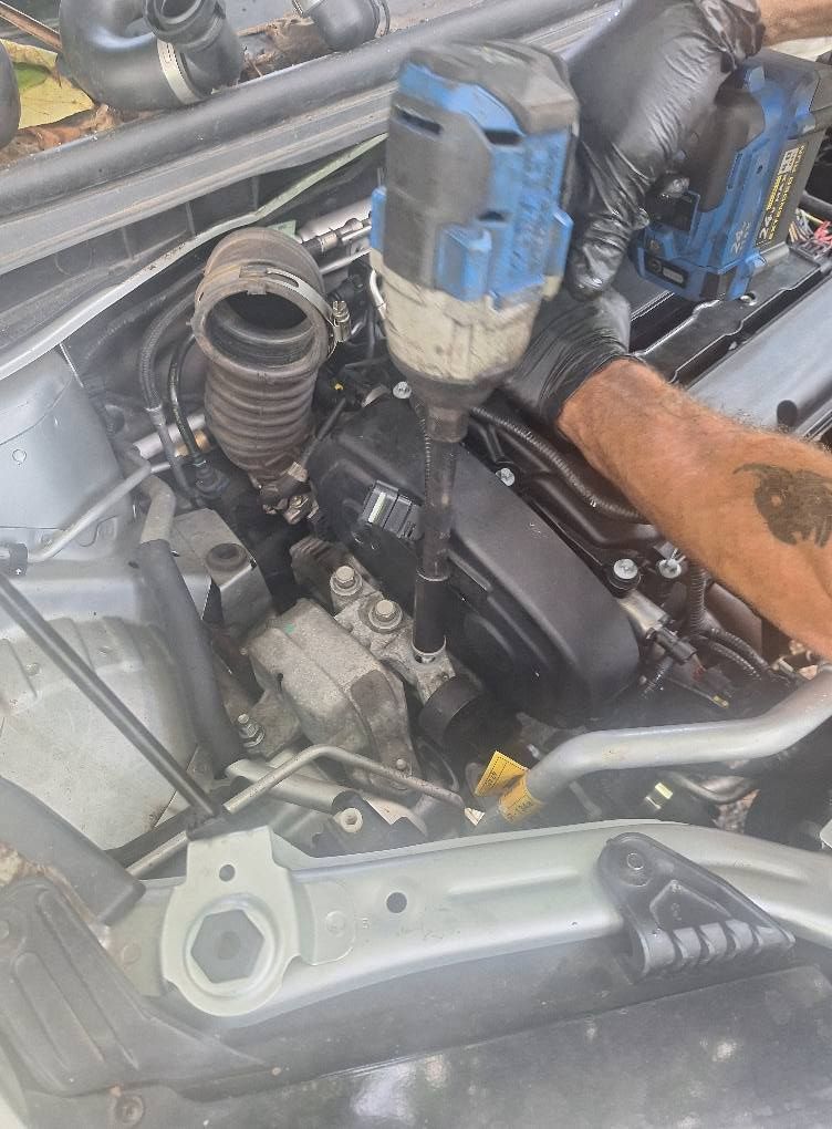 Mechanic using an impact wrench on a car engine, outdoors.