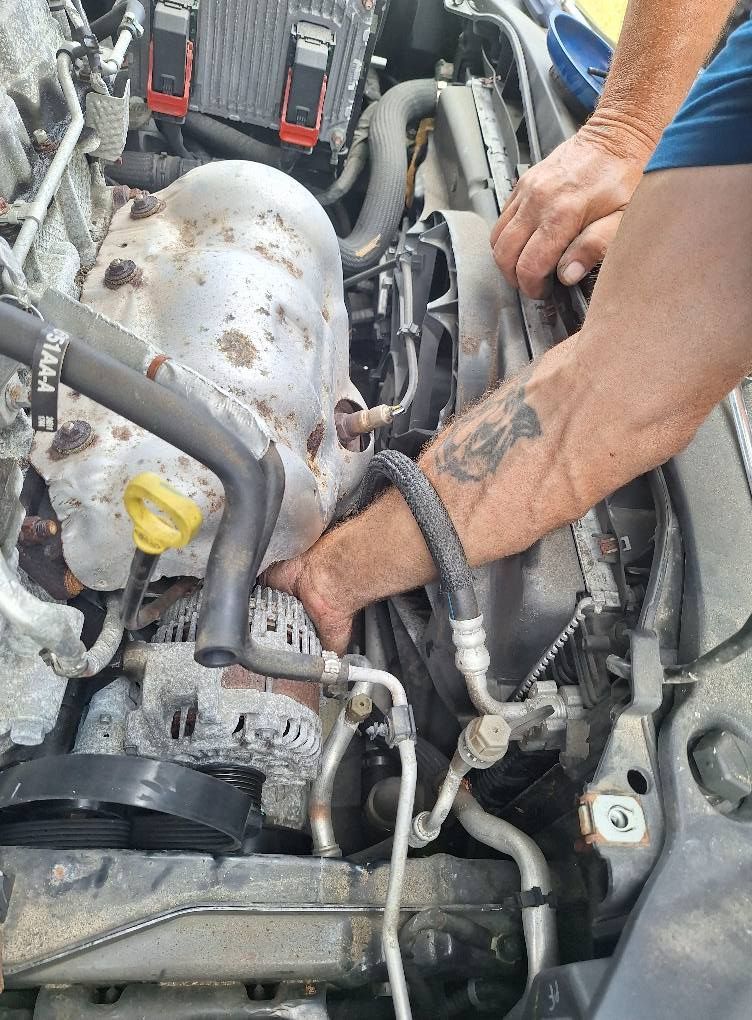 Hands working on a car engine; a person reaches in to work on engine parts.
