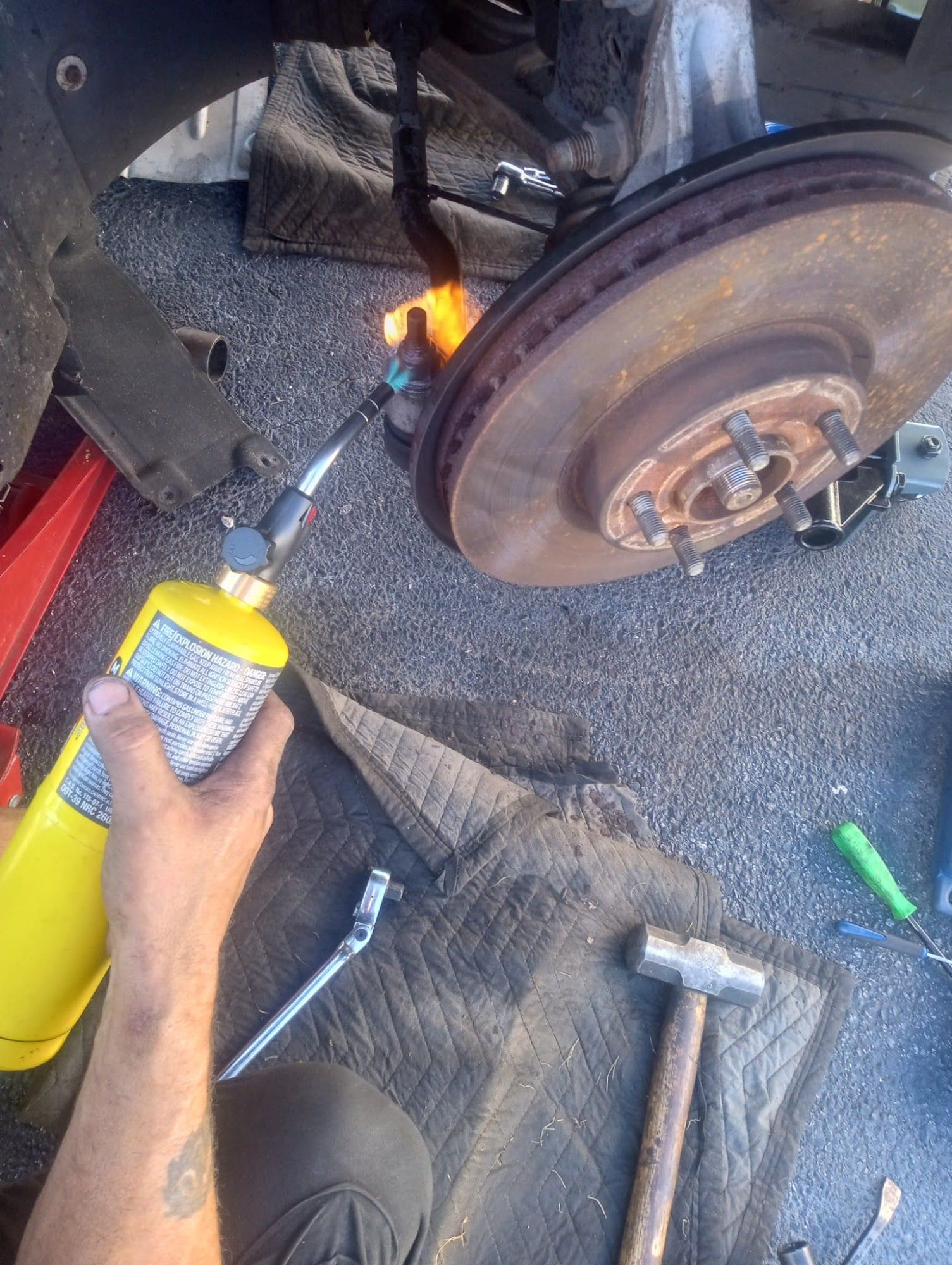 Person using a torch on a car brake rotor. A hammer and wrench are nearby.