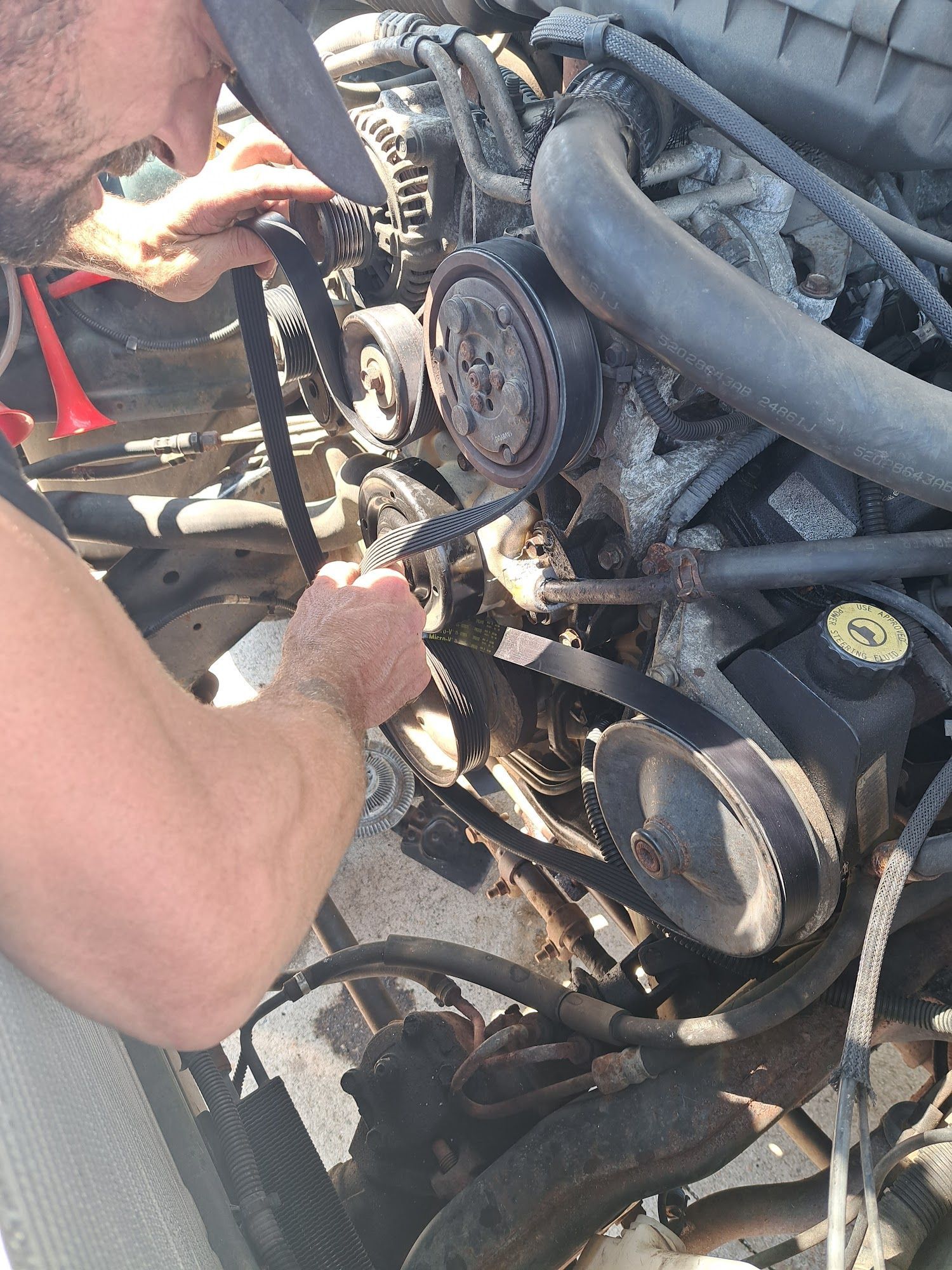 Person working on a car engine, examining a belt.