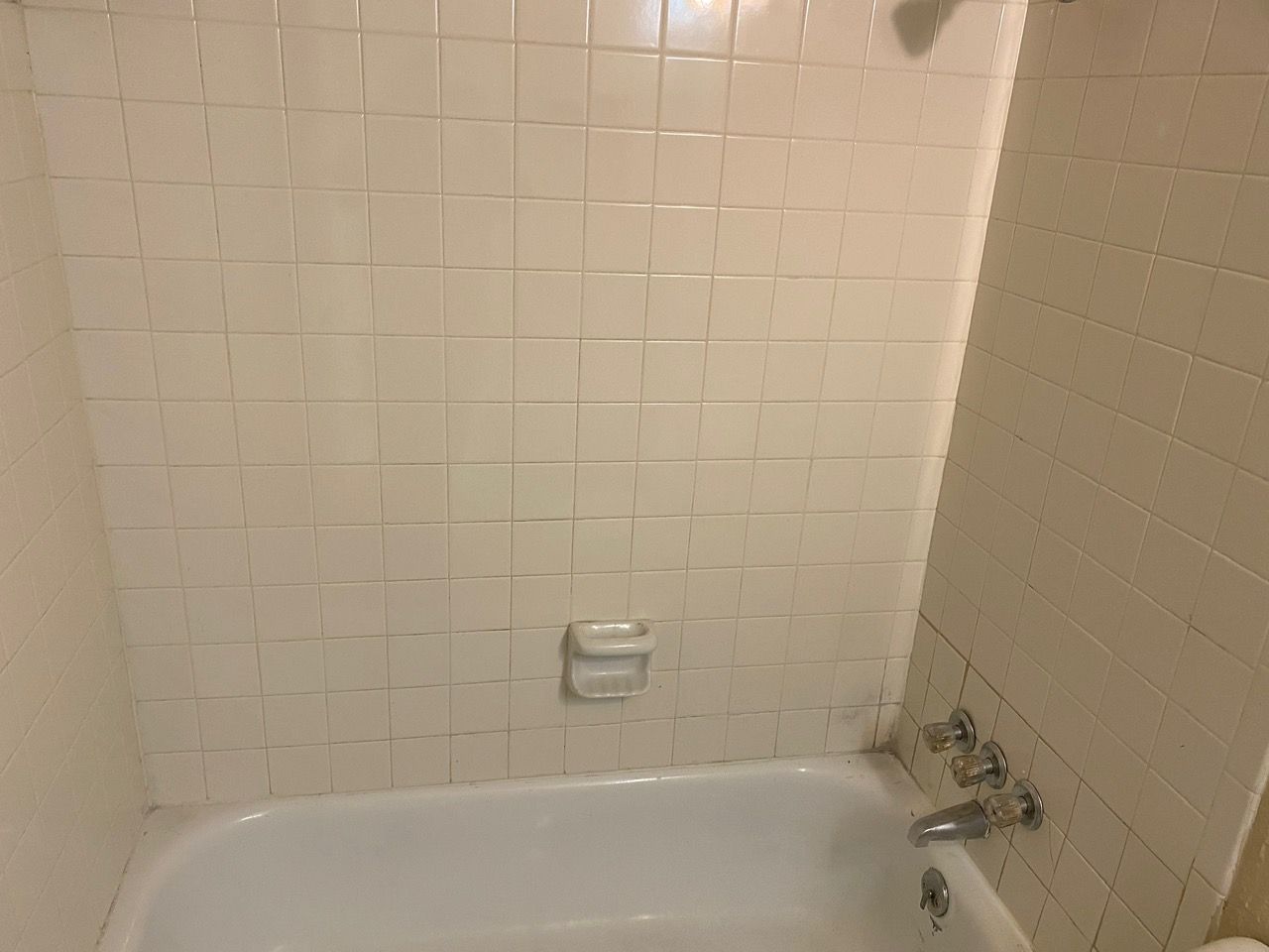White tiled shower with a bathtub and soap dish.