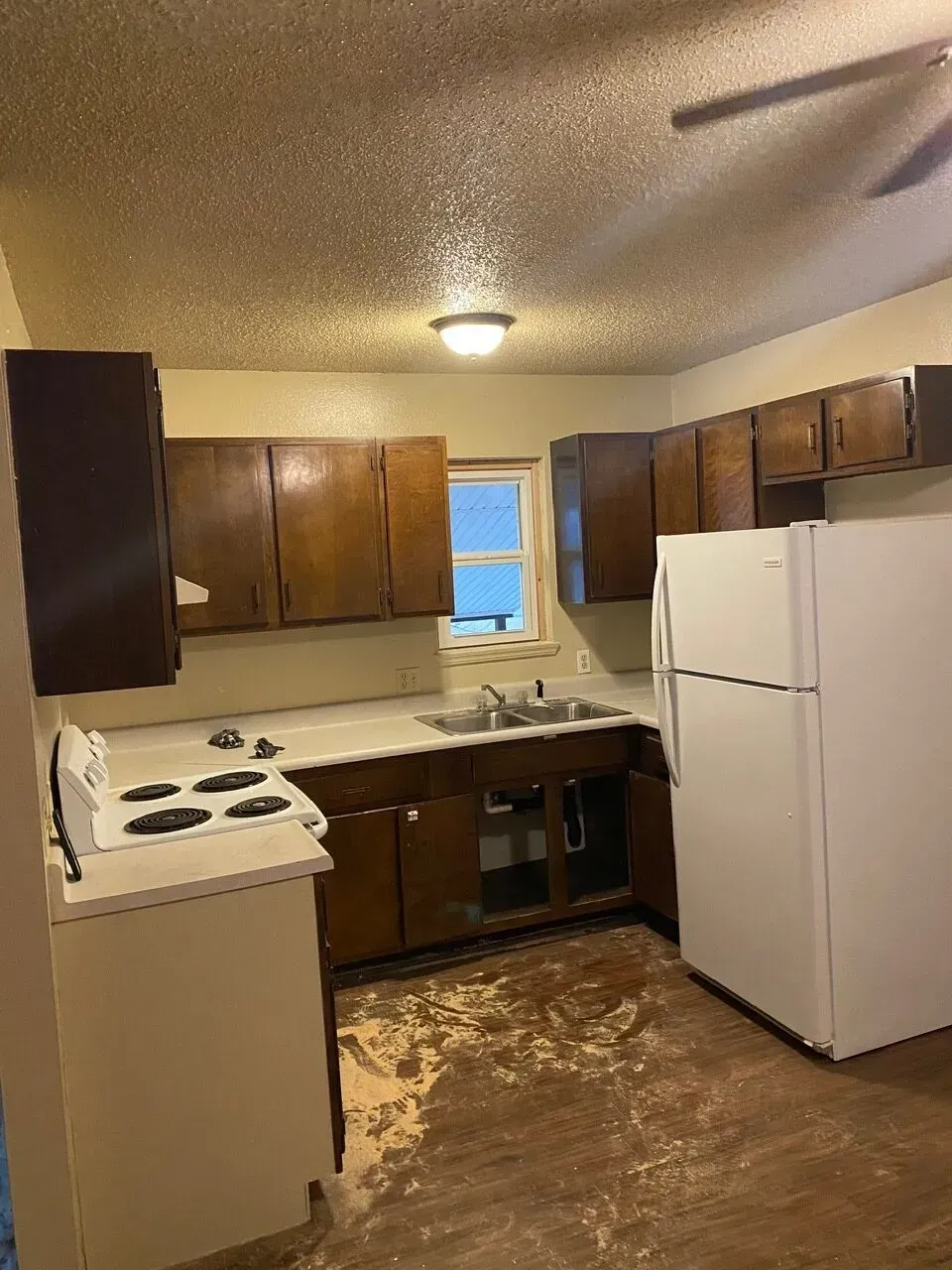 Brown kitchen cabinets, white appliances, and a stained floor in a room with a textured ceiling.