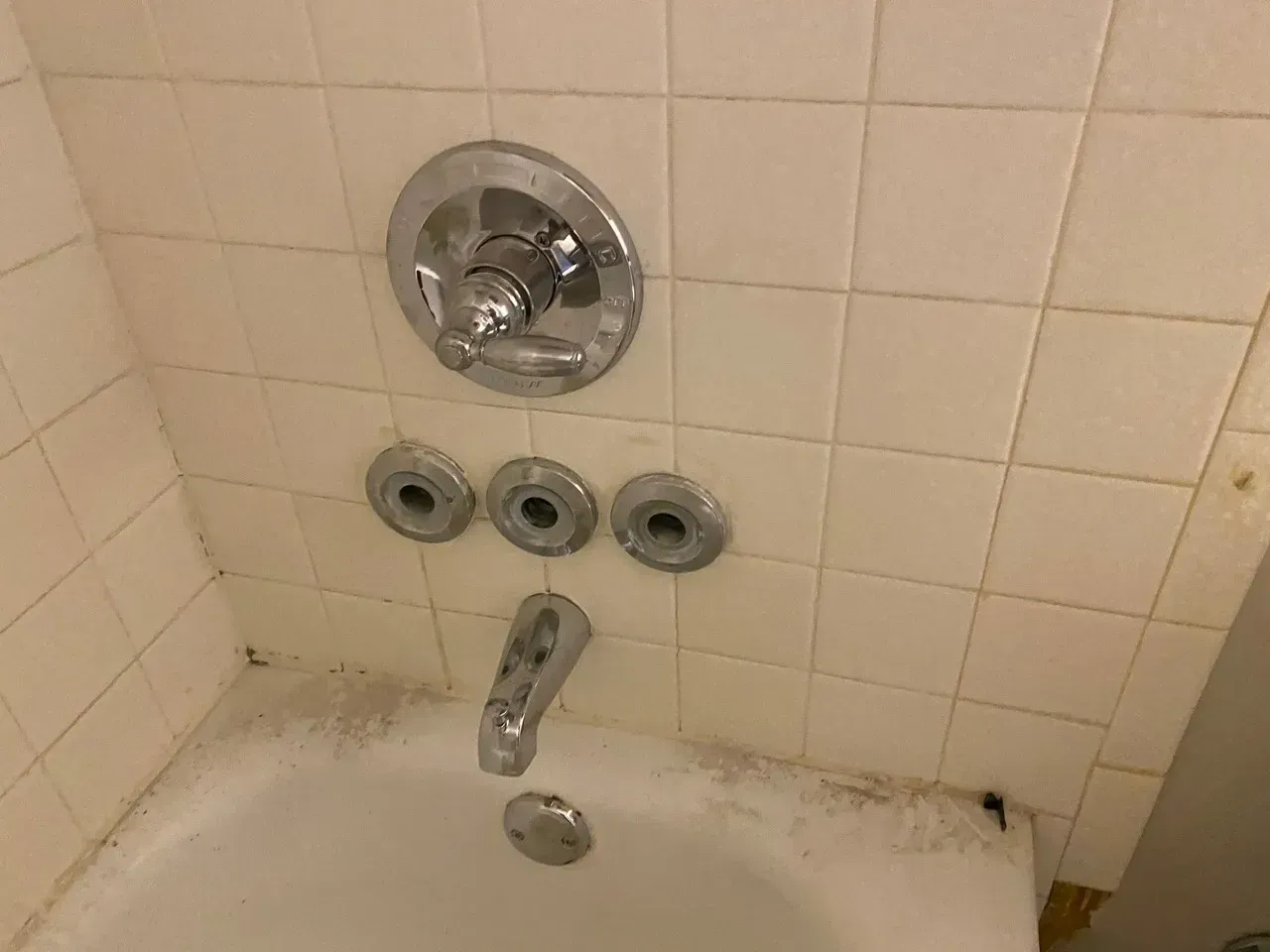 Bathtub with chrome fixtures on tiled wall. Faucet, showerhead, and three circular fixtures visible.