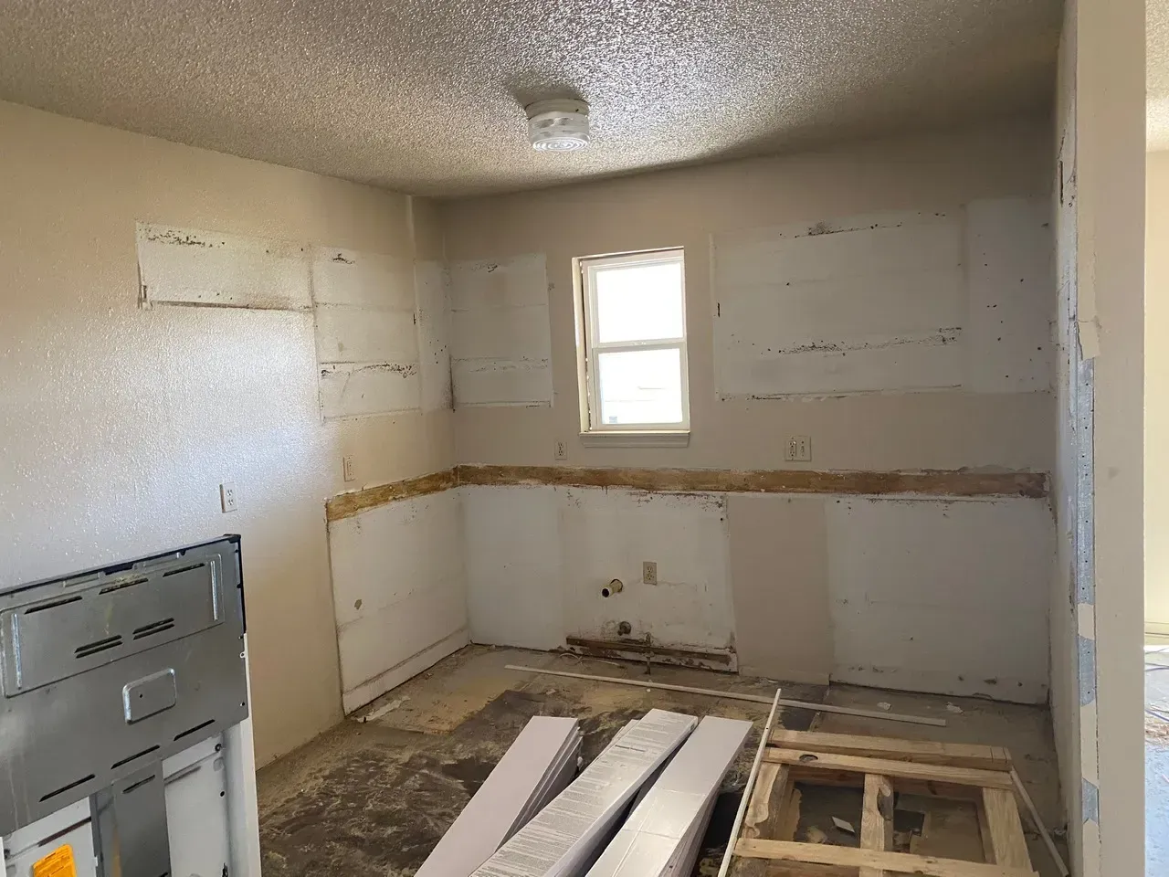 Interior kitchen under renovation; exposed walls, window, bare floor, drywall removed.