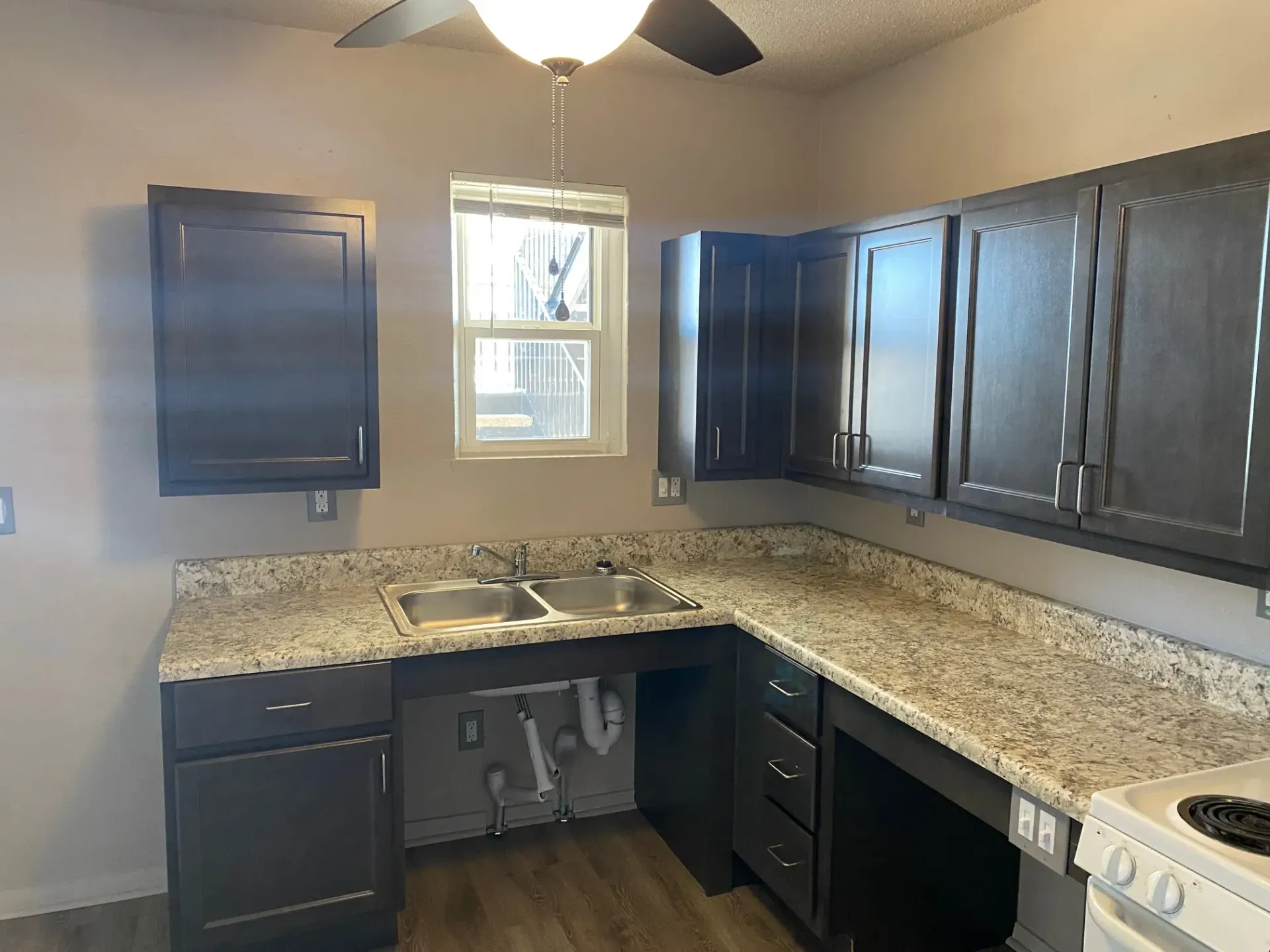 Dark-cabinet kitchen with granite countertops, a double sink, and a stovetop, featuring an accessible sink area.