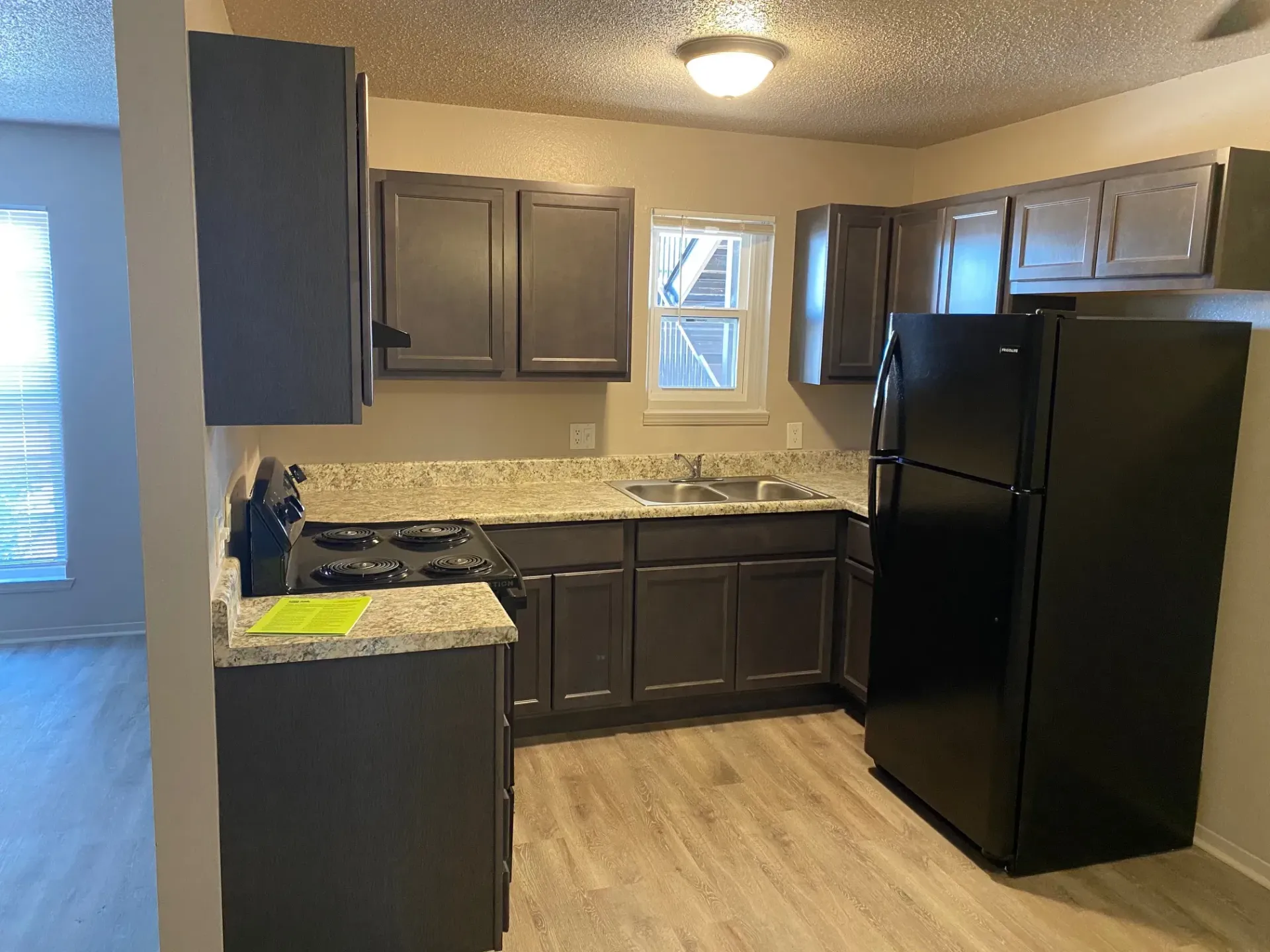 Kitchen with dark cabinets, granite countertops, black appliances, and light wood-look flooring.
