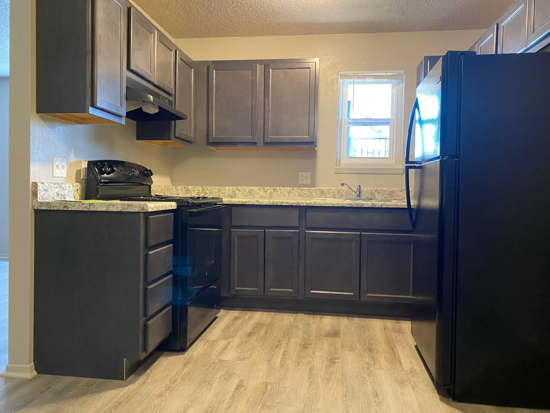 Kitchen with dark gray cabinets, black appliances, light countertops, and wood-look flooring.