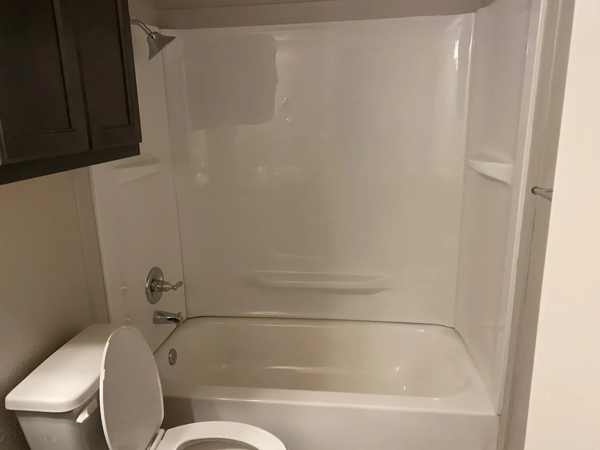 Bathroom with white tub, shower surround, toilet, and dark brown cabinet.