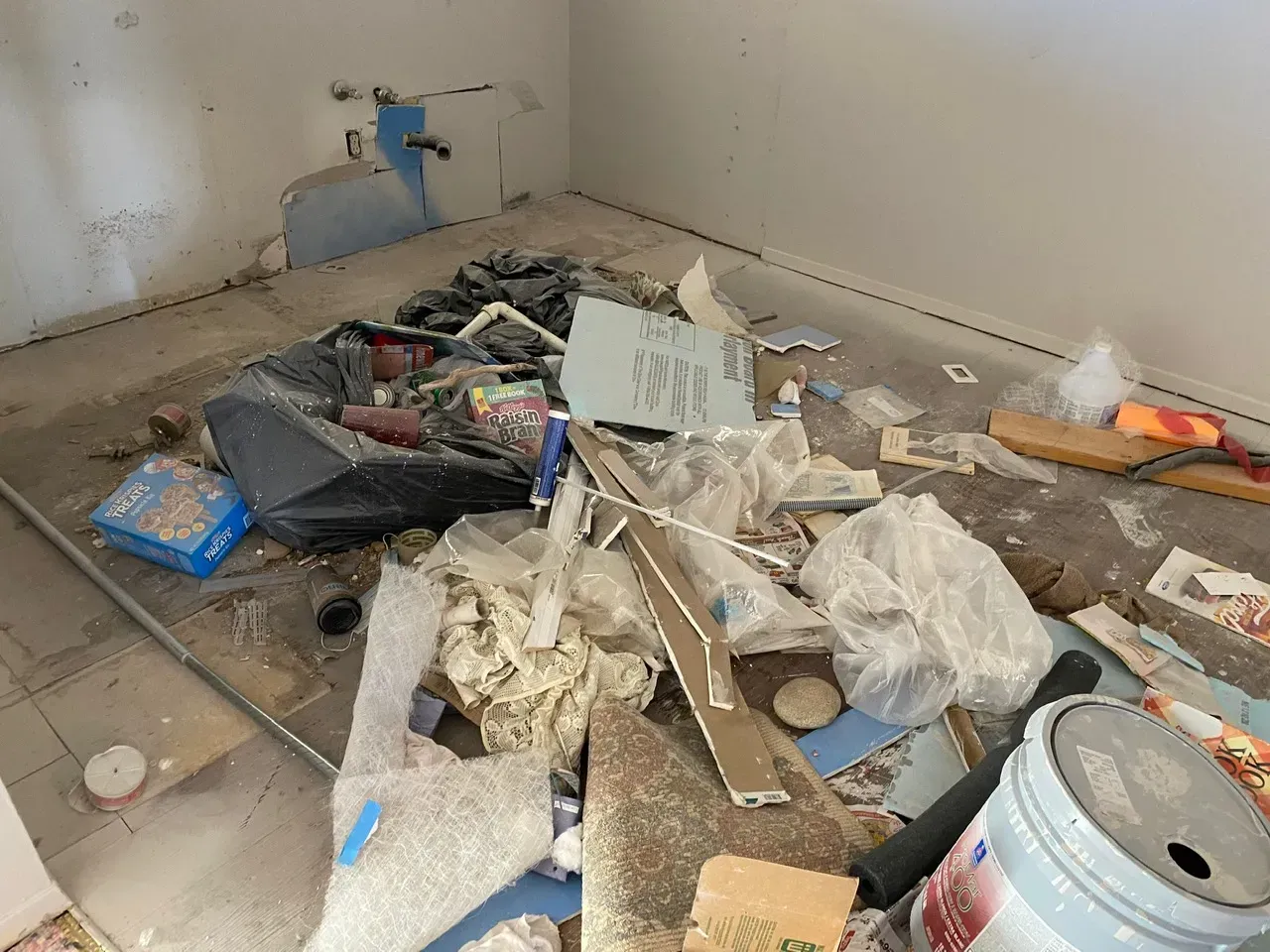 Messy room with construction debris, exposed pipes, and a paint bucket.
